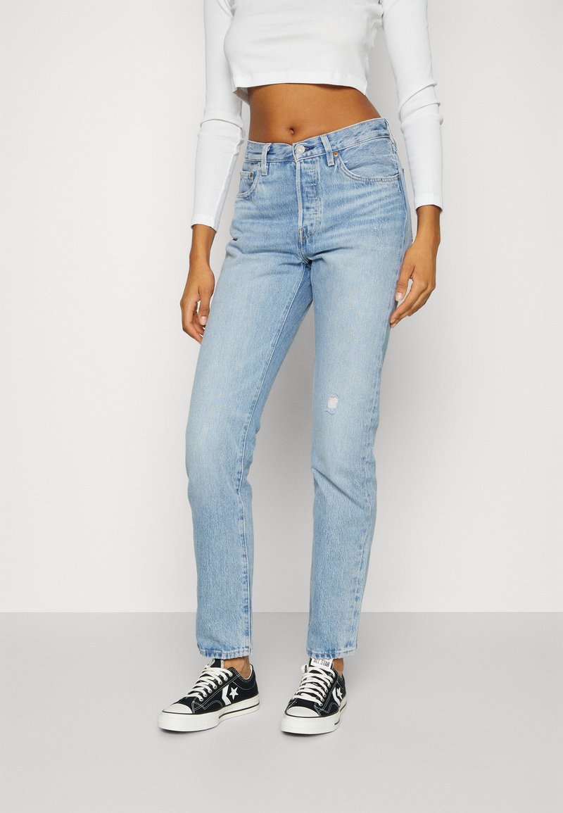 Jeans de mezclilla azul claro con cintura alta, corte recto y un ligero desgaste. Combinados con zapatillas bajas en blanco y negro.