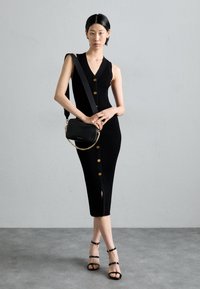 Černé žebrované midi šaty se zlatými knoflíky, mají hluboký V-výstřih a postranní rozparek. Doplněné černou kabelkou přes rameno a černými sandály na podpatku.