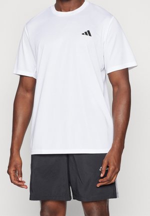 Man draagt een effen wit T-shirt met korte mouwen, voorzien van een klein zwart logo, en zwarte sportshorts met een witte streep en logo op het linkerbeen.