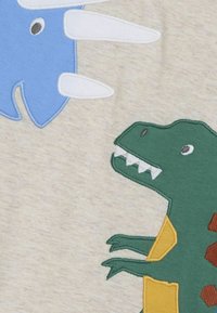 Gesticktes Dinosaurierdesign auf hellem Beigem Stoff; grüner T-rex mit gelben und braunen Akzenten, blauer Dinosaurier darüber mit weißen Stacheln.