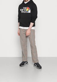 Felpa nera con cappuccio e logo "THE NORTH FACE" con arco colorato. Pantaloni a quadri in beige, arancione e blu marino, abbinati a sneakers nere.