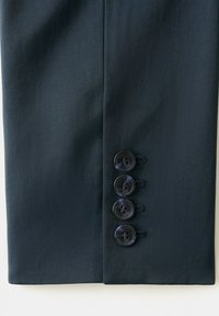 Dark navy suit sleeve with four black buttons arranged vertically near the cuff on textured fabric background.