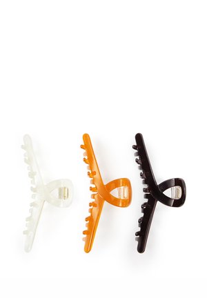 Tres clips de pinza para el pelo de plástico en blanco translúcido, naranja y marrón oscuro, dispuestos uno al lado del otro sobre un fondo blanco.