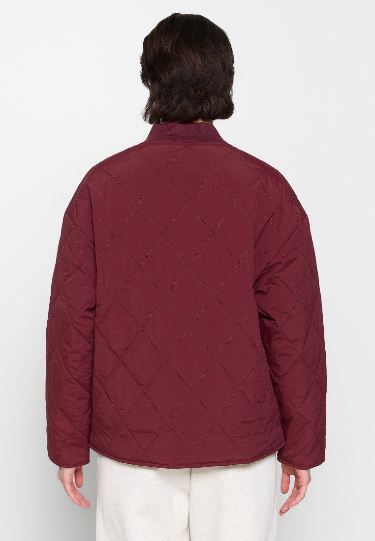Chaqueta acolchada color burdeos con cuello redondo y patrón en diamante. Presenta un corte relajado y una textura de tela suave. Vista trasera lisa.