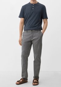 Marinblå henley-tröja med tre knappar, ljusgrå mönstrade byxor och bruna sandaler med remdesign. Båda delarna är avslappnade och andningsbara.