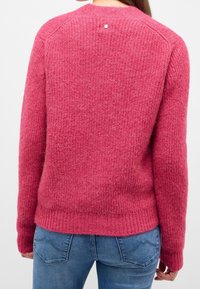 Rosa stickad tröja med ett strukturerat mönster, ribbad nederkant och manschetter. Har en liten dekorativ knapp i nacken bak.