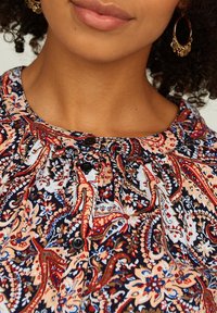Blusa con motivo a fantasia caratterizzata da vivaci design paisley in rosso, blu navy e crema; scollatura rotonda con texture arricciata e bottoni neri.