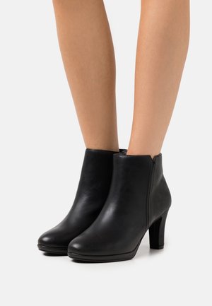 Bottines en cuir noir avec un bout rond, un talon effilé et des détails de fermeture éclair sur le côté. Texture lisse avec un design minimaliste.