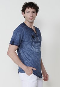 T-paita, jossa on lyhyet hihat, rento istuvuus, pyöreä kaula-aukko, osittainen nappilista ja painettu graafinen kuvitus edessä.