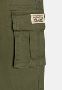 Tessuto cargo verde oliva con una tasca laterale e un'etichetta cucita che presenta il classico logo Levi Strauss & Co. Visibili dettagli cuciti e texture.