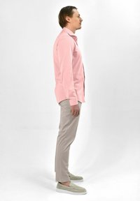 Lichtroze langes shirt met lange mouwen, op maat gemaakt, met een button-down kraag. Gecombineerd met beige slim-fit broeken en lichtgrijze instappers.