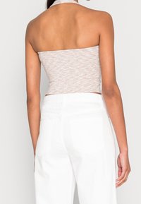 Kvinna som bär en beige strapless topp och högmidjade vita byxor, sedd bakifrån mot en enkel bakgrund.