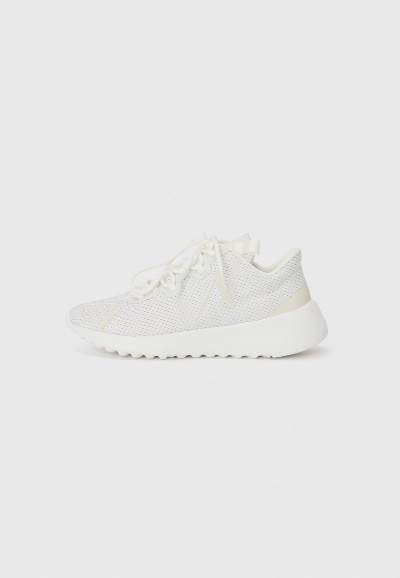 White athletic shoes with a mesh upper, textured surface, and rubber sole. Features thin laces and subtle cream accents on the heel.