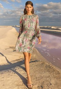 Rochie mini florală în verde deschis cu accente roz și argintii, având mâneci lungi, talie elastică și un siluetă fluidă.