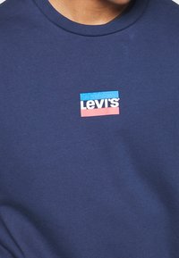 T-shirt bleu marine avec petit logo Levi's en texte blanc, centré entre une barre rectangulaire bleue et une rouge sur la poitrine.