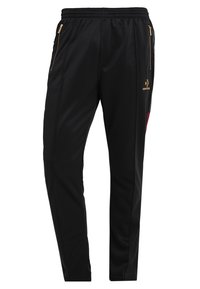 Musta urheiluhousut, joissa on kultaiset vetoketjulliset taskut, joustava vyötärö ja pieni kultainen Converse-logo vasemmalla reiden yläosassa.