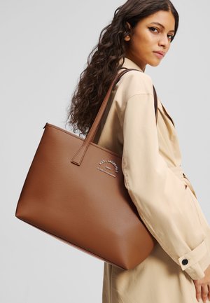 Brown faux leather tote bag with a structured shape, featuring a logo accent. It has two shoulder straps and a smooth texture.