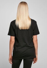 Černé tričko s krátkým rukávem vyrobené z bavlny, volný střih; pohled zezadu s zakulaceným spodním lemem a přímými stehy.