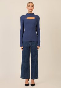 Maglione a coste blu navy con collo alto e dettaglio con taglio, abbinato a jeans in denim a gamba larga con sottili applicazioni di borchie, indossato con tacchi neri.