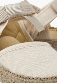 Espadrille de lona con parte superior beige, ribete de yute y detalle de lazo texturizado en la correa. Suave acolchado interior de color neutro.