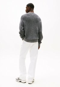 Pullover grigio lavorato a maglia con motivo testurizzato, abbinato a jeans bianchi a taglio morbido e sneaker con motivo. Vista da dietro.