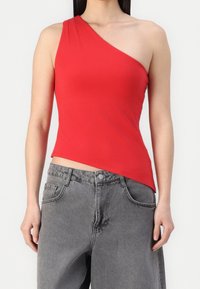 Rode top met één schouder, gemaakt van een gladde, rekbare stof. Strak design met een asymmetrische zoom, gecombineerd met vervaagde grijze baggy jeans.