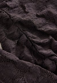 Tmavá krajka s propracovanými květinovými vzory a výřezy, ukazující texturovaný povrch s měkkým splývavým efektem.
