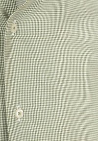 Lichtgroene en witte houndstooth-geprinte stof met twee crèmekleurige knopen die gedeeltelijk zichtbaar zijn langs een naad.