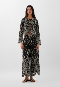 Zwart geborduurd twee-delig set bestaande uit een cropped jas met lange mouwen en brede broek, versierd met bloem- en paisleypatronen.