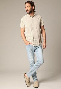 Chemise à manches courtes, de couleur claire, avec un motif à pois, associée à un jean bleu clair et des chaussures slip-on beiges.