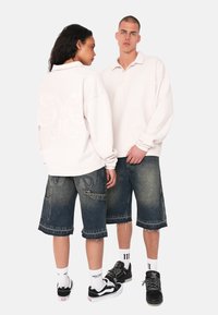 Lyserød broderet sweatshirt med krave, parret med mørkeblå denimshorts med frynset kant og sidelommer. Sorte sneakers inkluderet.