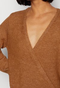 Brun stickad tröja med djup V-ringning och avslappnad passform. Mjuk textur, ribbad halsringning och något överdimensionerade ärmar.