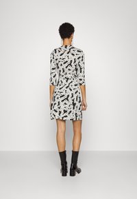 Svart klänning med vitt abstrakt mönster, trekvartsärmar, figurnära midja, mitt-lår längd, i kombination med svarta knähöga stövlar.