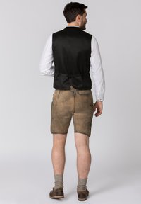 Schwarze Stoffweste über einem weißen Hemd, kombiniert mit braunen Leder-Shorts. Die Shorts haben Seitentaschen und eine strukturierte Oberfläche mit einem Kordelzugbund.