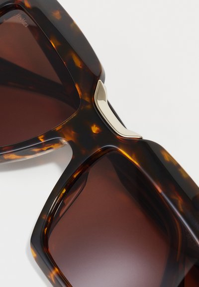 Lunettes de soleil écaille de tortue avec une forme carrée, des verres brun dégradé, et un accent métallique sur la monture pour une touche de détail supplémentaire.