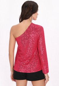 Asymmetrisk top med én skulder i lysende pink pailletstof, langærmet på den ene side, parret med sorte shorts. Glat tekstur med skinnende detaljer.