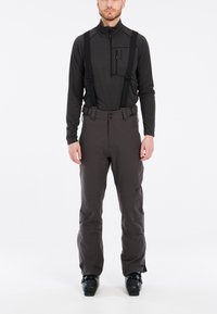 Dunkelgraue Skihosen mit verstellbaren schwarzen Trägern, einer vorderen Reißverschlusstasche und einer glatten, matten Textur, kombiniert mit einem schwarzen Langarmshirt.