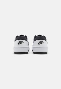 Baskets Nike avec une tige en cuir blanc, des accents en suède noir et une semelle en caoutchouc. Présente un logo noir au niveau du talon et un design épuré.