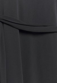 Tissu gris foncé au toucher lisse, présentant un détail noué qui crée une apparence enveloppante. Le design est minimaliste et harmonieux.