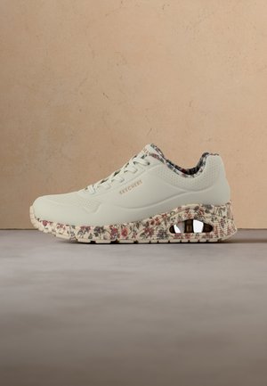 Biały sneaker Skechers z kwiatowym wzorem na podeszwie i wkładce, sznurowany i z nazwą marki z boku.