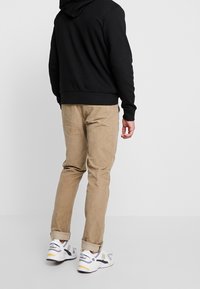 Sudadera negra para hombre, pantalones de pana beige y zapatillas deportivas blancas con acentos grises y amarillos. Enfocado en ropa casual y cómoda.