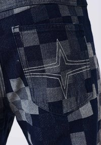 Bolsillo trasero de pantalones a cuadros en tonos azul oscuro y gris, con un detalle de costura blanca en forma de estrella.