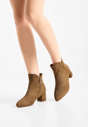 Donna che indossa stivaletti marroni in suede con tacco a blocco e zip laterali su sfondo bianco.