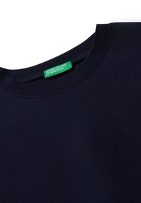 Námořnická modrá tričko s kulatým výstřihem a zelenou textilní etiketou s nápisem "United Colors of Benetton" přišitou uvnitř límce.