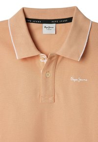 Polo shirt pesca con un tessuto testurizzato, dettagli in bianco sul colletto, una chiusura a bottoni e un piccolo logo ricamato sul petto.