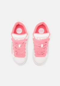 White sneakers with pink accents and thick, textured pink laces. Soft interior lining with a circular logo on the tongue. Modern, sporty design.