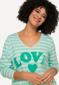 Randig långärmad topp i mintgrön och vit, med överdimensionerad text "LOVE" i texturerad turkos med ett hjärtmotiv, V-ringning.