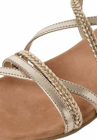 Sandales à brides tressées dorées avec une semelle intérieure en daim doux et une semelle plate. Comprend des accents tissés et une finition métallique brillante.