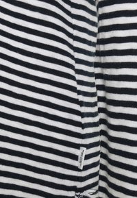 Tela a rayas en blanco y negro, con rayas finas y gruesas. En el borde se puede ver una etiqueta de prenda que indica el nombre de la marca.