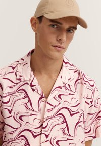 Kurzarmhemd aus weichem rosa Stoff mit einem wirbelnden burgunderfarbenen Muster. Verfügt über eine Knopfleiste und ein klassisches Kragendesign.